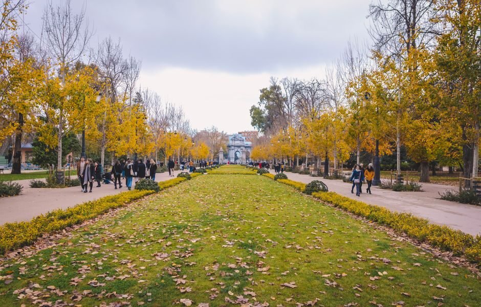 Una escena vibrante de otoño en el Parque del Retiro, Madrid, con personas caminando entre árboles coloridos.