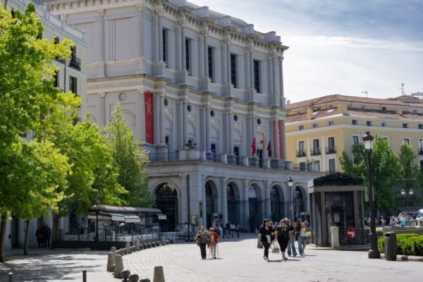 Vista diurna del Teatro Real de Madrid, con gente paseando bajo un cielo despejado.