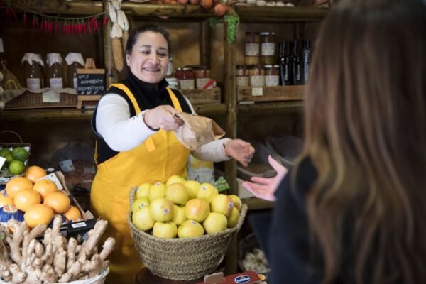Mujer vendedora sonriente entregando una bolsa a un cliente en una tienda de comestibles en Madrid.