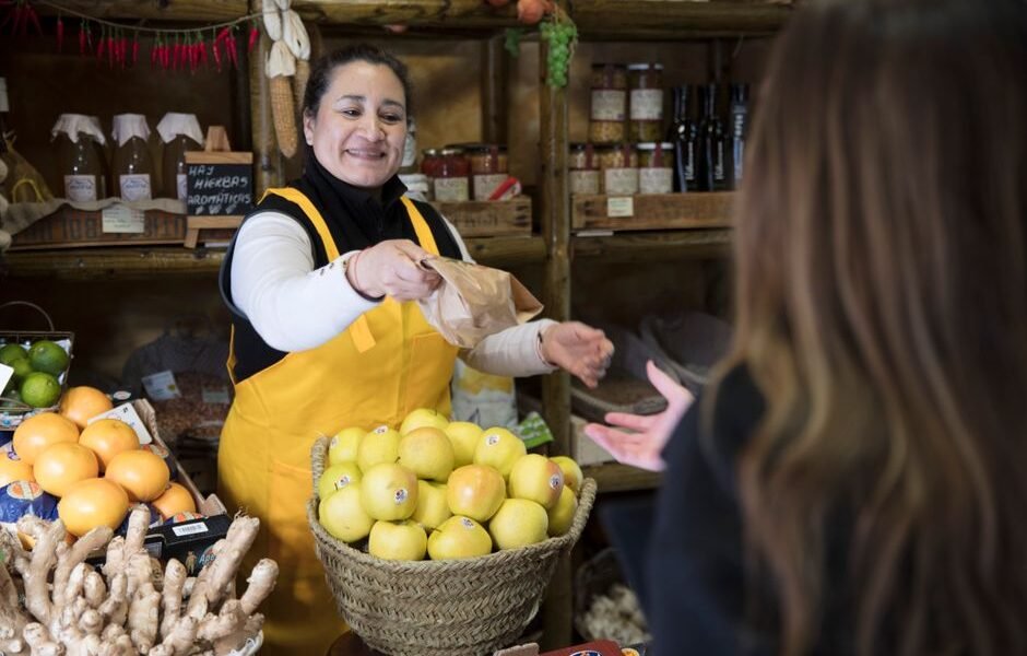 Mujer vendedora sonriente entregando una bolsa a un cliente en una tienda de comestibles en Madrid.