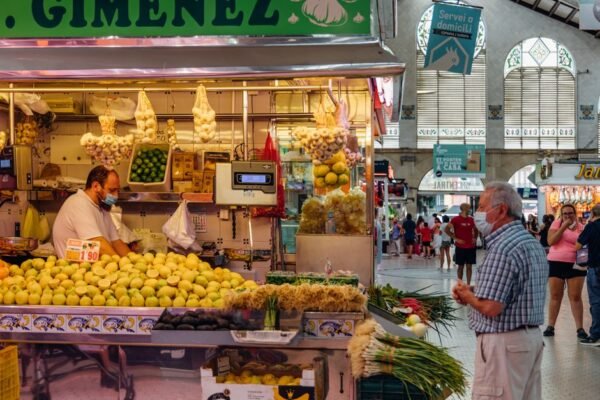 Un concurrido puesto de mercado en Valencia, España, con productos frescos y gente comprando.