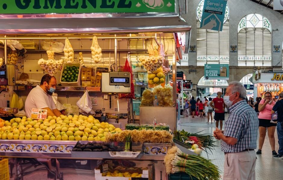 Un concurrido puesto de mercado en Valencia, España, con productos frescos y gente comprando.